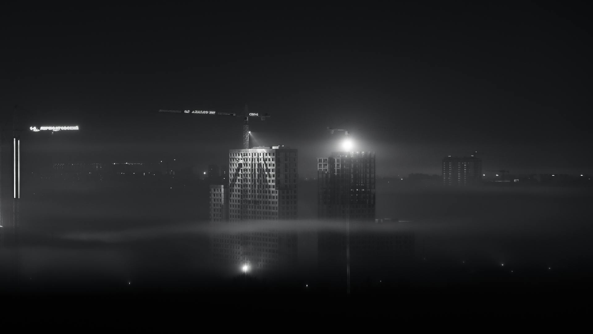 A foggy night view of Moscow's modern skyline with illuminated buildings and construction cranes.